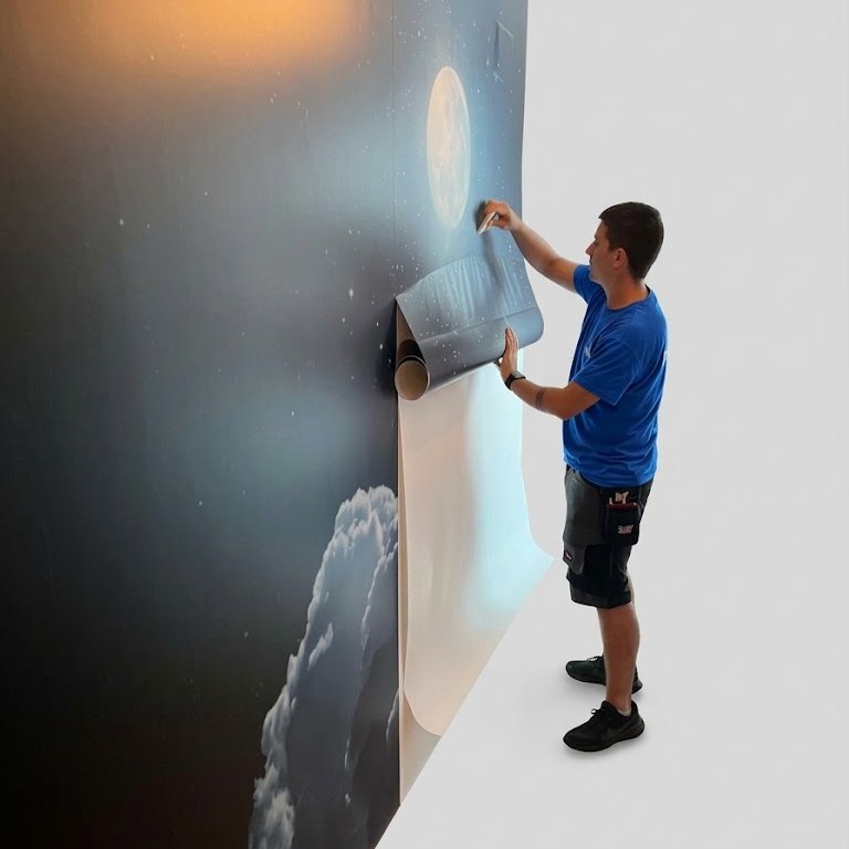 Técnico de Delta colocando un vinilo mural de gran formato con un cielo nocturno, la luna y nubes