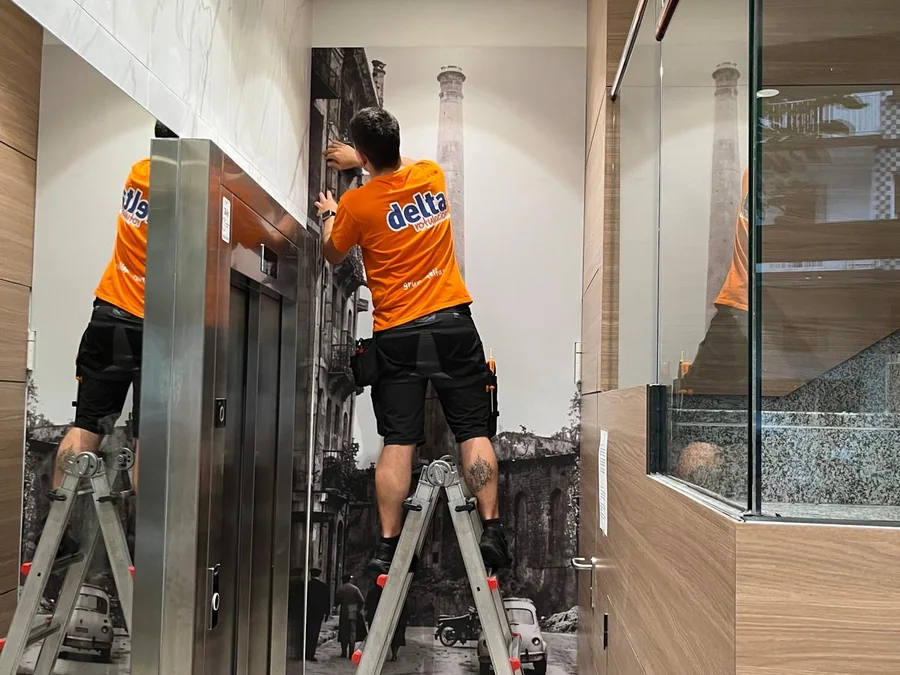 Instalador de Delta colocando un mural vinilado con una fotografía antigua de la ciudad en el portal de un edificio
