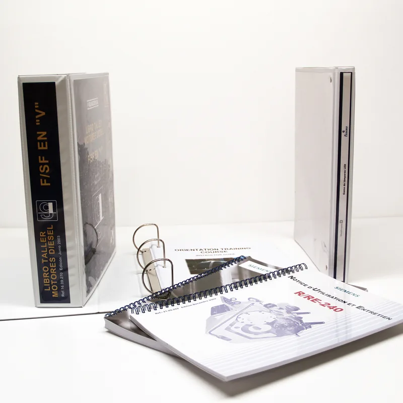 Manuales técnicos reales en archivador, wire-o y grapado sobre mesa blanca